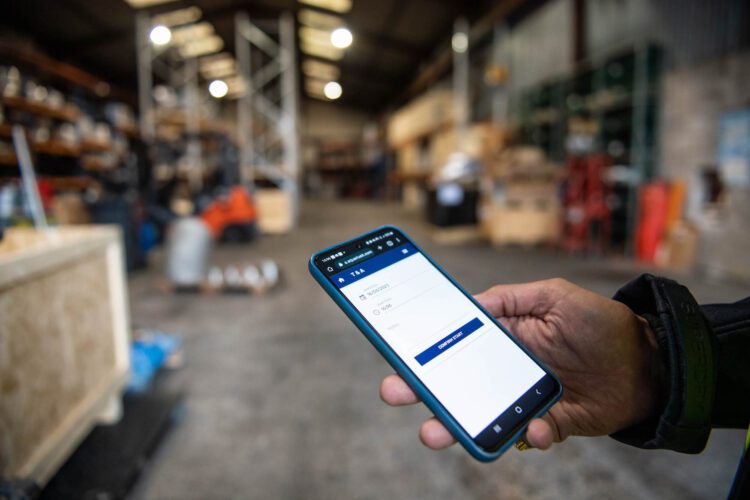 Hand Holding Phone With Aquarius IT App In A Warehouse